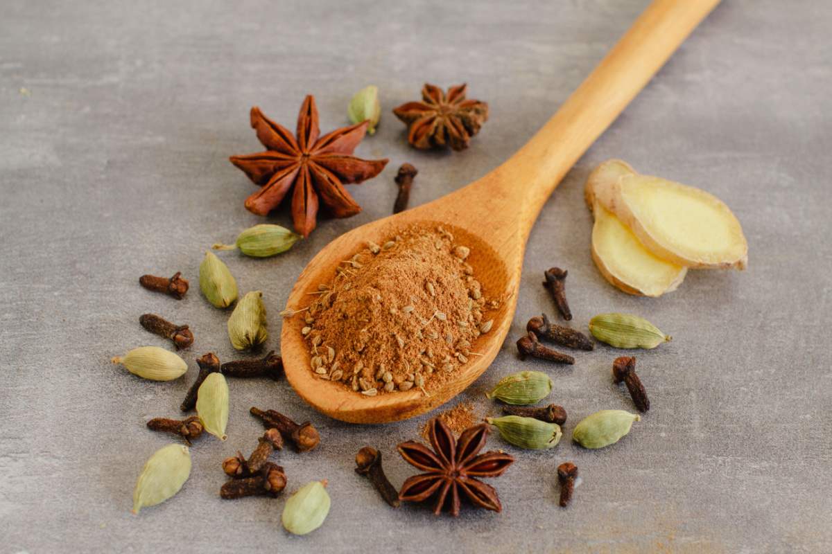 A collection of different spices used for infusing spiced rum including cloves, cardamom, star anise, ginger and cinnamon which is being held in a spoon.