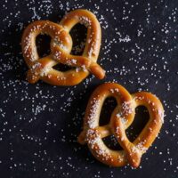 Two homemade pretzels on a black background that is filled with grains of salt.