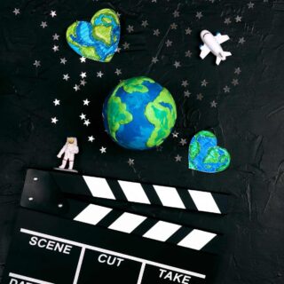 A film clapper with a tiny astronaut, space ship, and images of the earth nestled among the stars above it to symbolize and celebrate Earth Day.