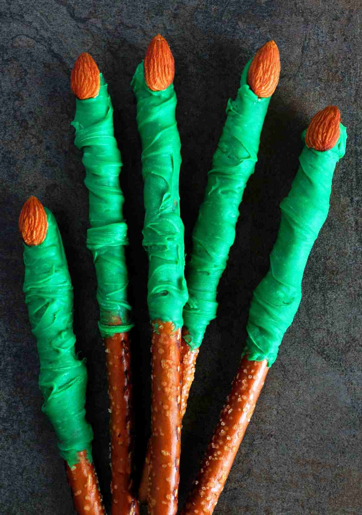 Green witch fingers pretzel rods arranged to look like a hand, with raw almonds as the nails, and green frosting as the witches skin.