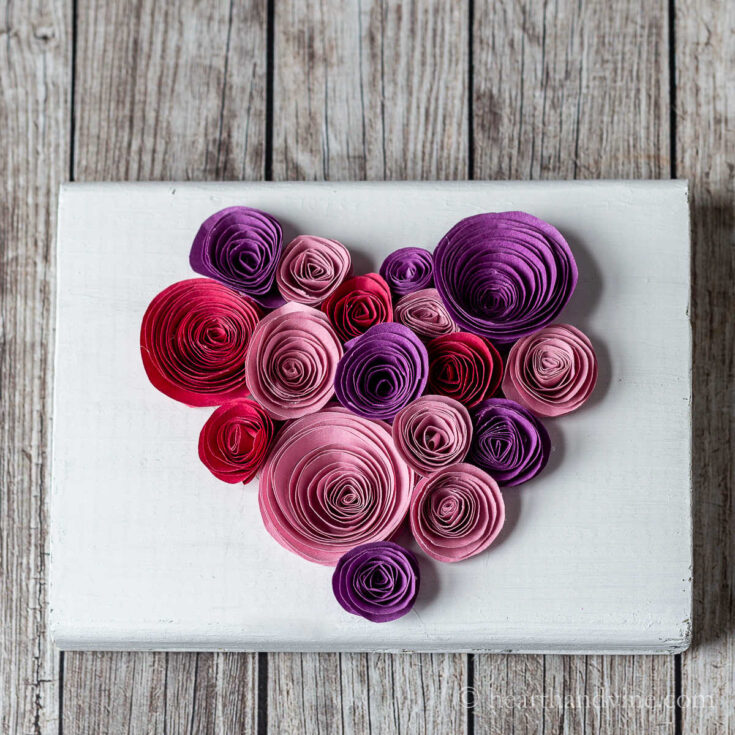 Paper rolled into circles in a heart shape on a block of wood.