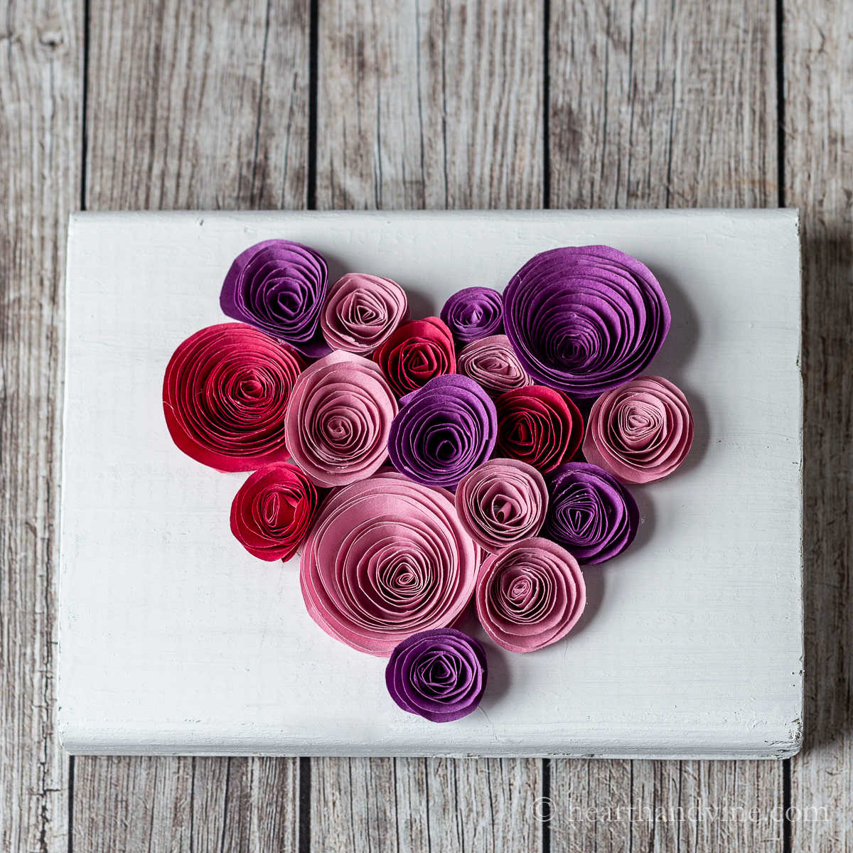Paper rolled into circles in a heart shape on a block of wood.