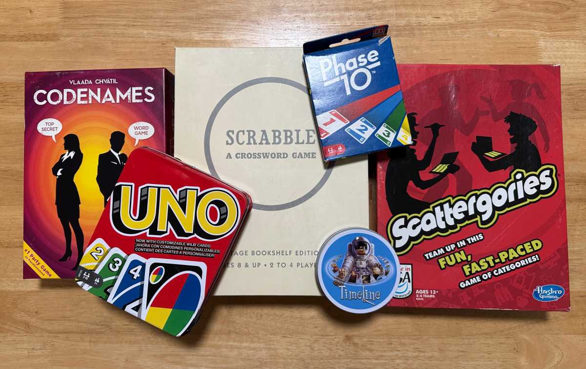 Six board games on a wooden table, including Code Names, Uno, Scrabble, Phase 10, Timeline and Scattergories.