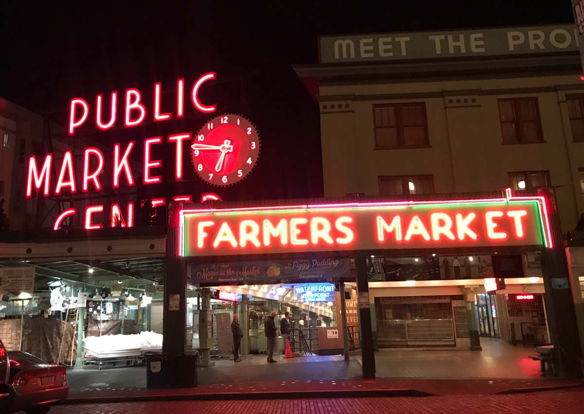 The outside view of the Pike Place Farmer's Market at night, where the signs are lit up.