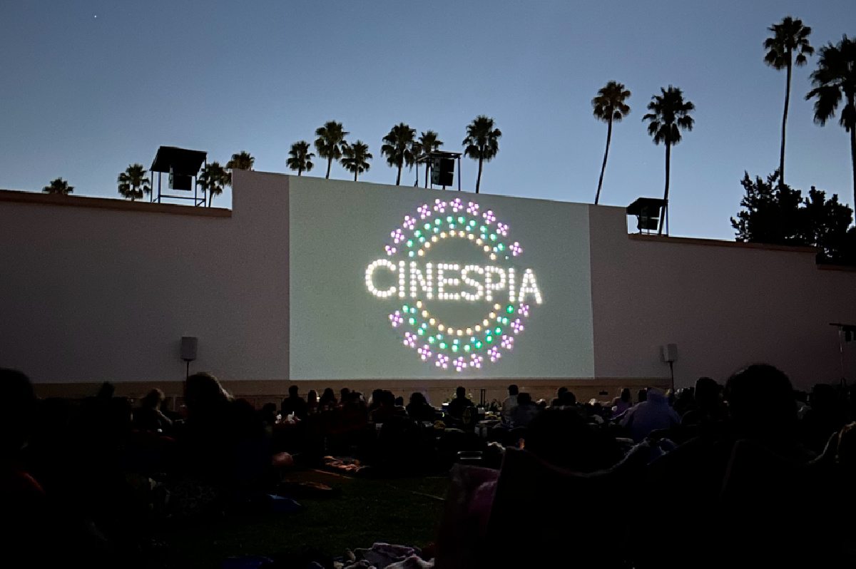 An outdoor summer movie screening in the Hollywood Forever Cemetery in Los Angeles, California, with the name Cinespia projected on the wall.