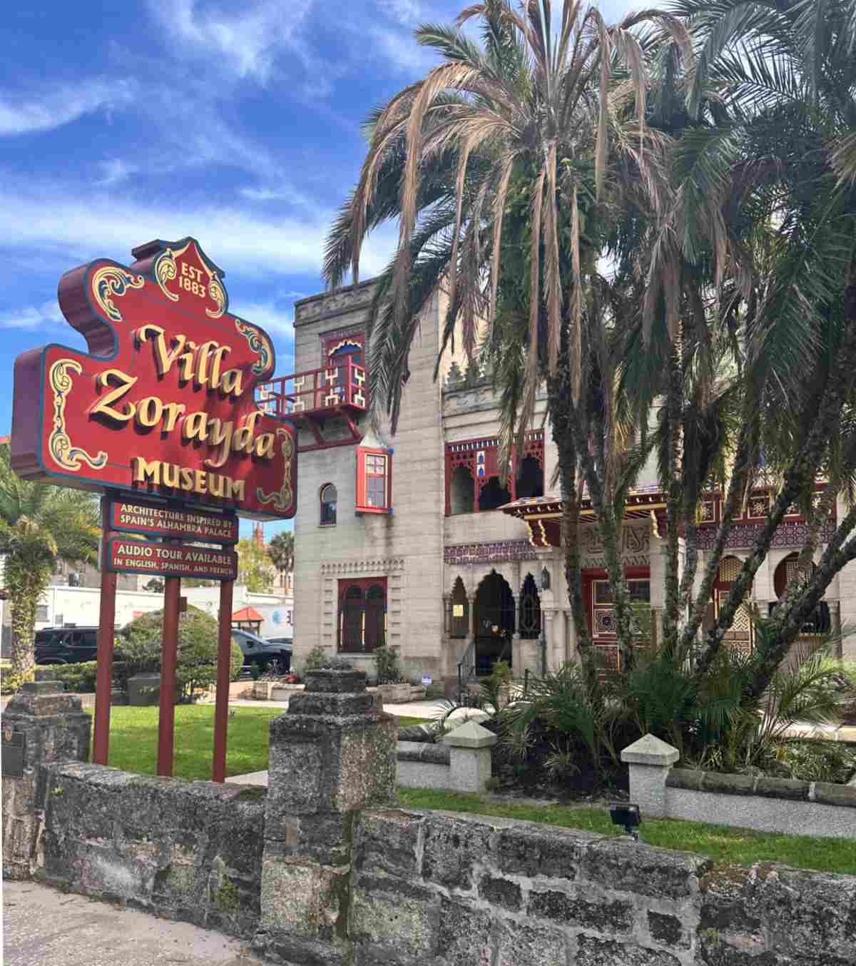 An outside video of St. Augustine Florida's Villa Zorayda Museum and its sign from the road, and the building is partially blocked by a clump of palm trees.